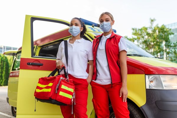 two female paramedics standing by the ambulance. two emergency nurses with face mask. paramedic carrying a medical trauma bag