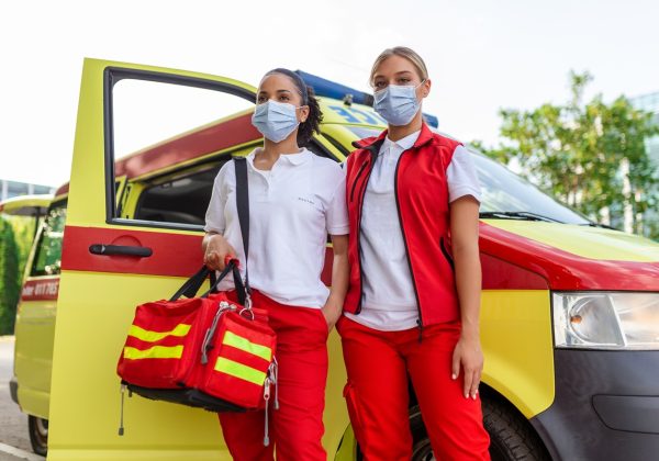 two female paramedics standing by the ambulance. two emergency nurses with face mask. paramedic carrying a medical trauma bag