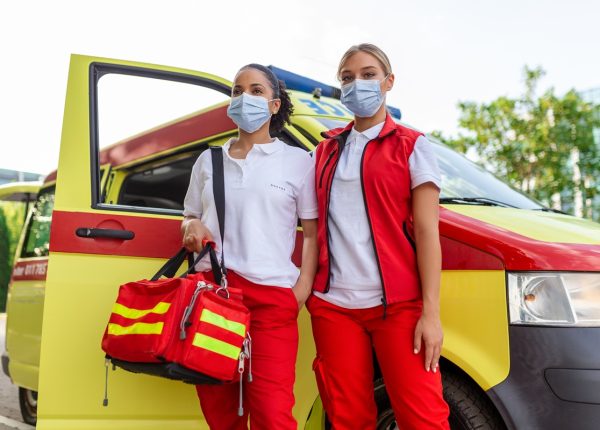 two female paramedics standing by the ambulance. two emergency nurses with face mask. paramedic carrying a medical trauma bag