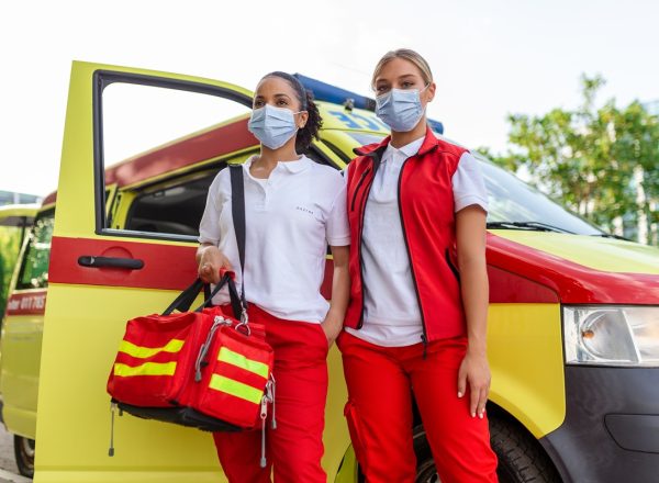two female paramedics standing by the ambulance. two emergency nurses with face mask. paramedic carrying a medical trauma bag