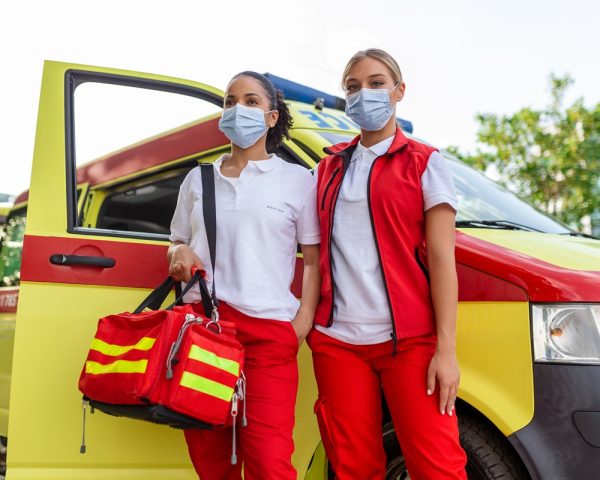 two female paramedics standing by the ambulance. two emergency nurses with face mask. paramedic carrying a medical trauma bag